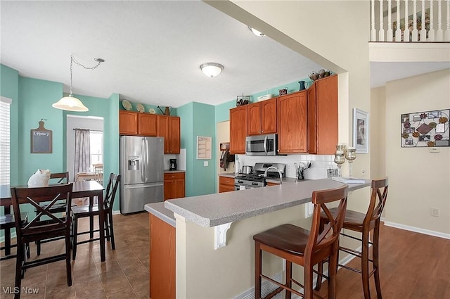 kitchen with brown cabinetry, a breakfast bar area, light countertops, a peninsula, and appliances with stainless steel finishes