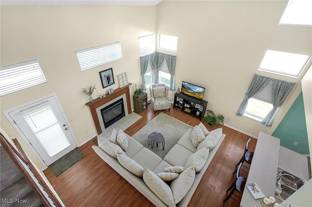 living area with a fireplace with flush hearth, wood finished floors, and high vaulted ceiling
