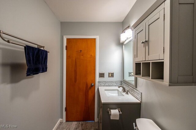 half bath with baseboards, wood finished floors, toilet, and vanity
