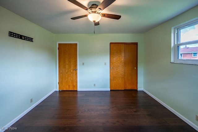 unfurnished bedroom featuring baseboards, a ceiling fan, dark wood-type flooring, and a closet