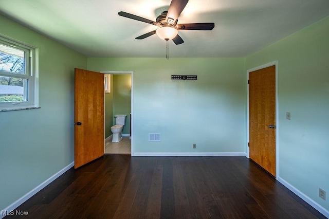 unfurnished bedroom featuring dark wood-style floors, baseboards, ensuite bathroom, and visible vents