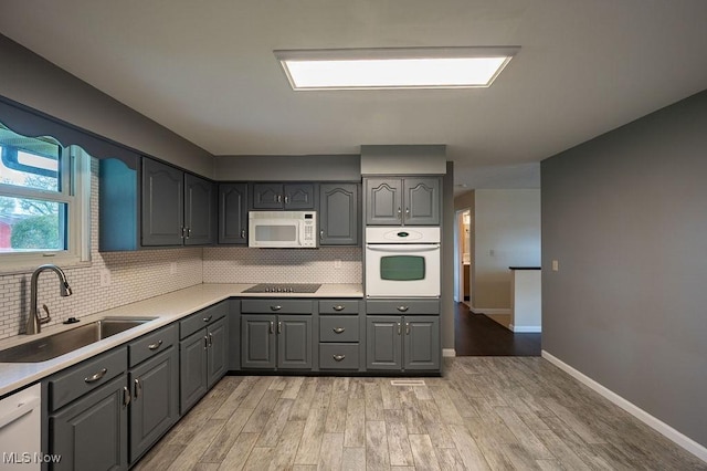 kitchen featuring decorative backsplash, gray cabinetry, white appliances, and a sink