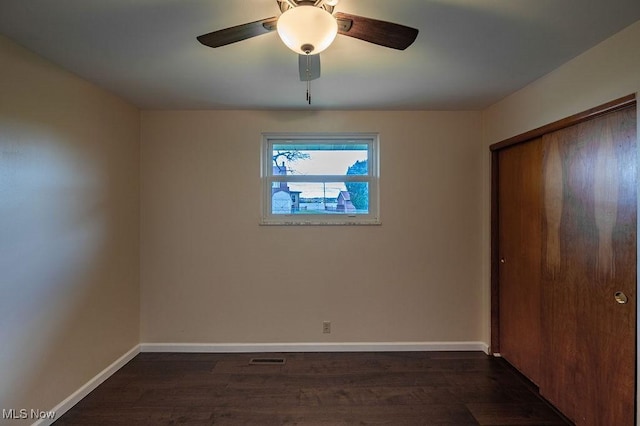 unfurnished bedroom featuring dark wood-type flooring, a closet, baseboards, and visible vents