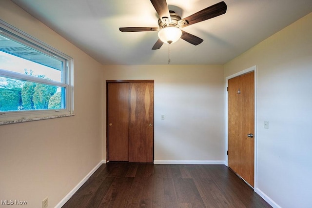 unfurnished bedroom with dark wood finished floors, a closet, baseboards, and ceiling fan