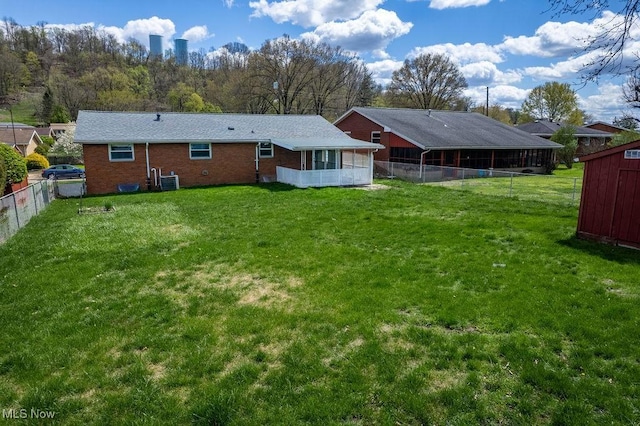 rear view of house with fence, a lawn, a sunroom, and brick siding