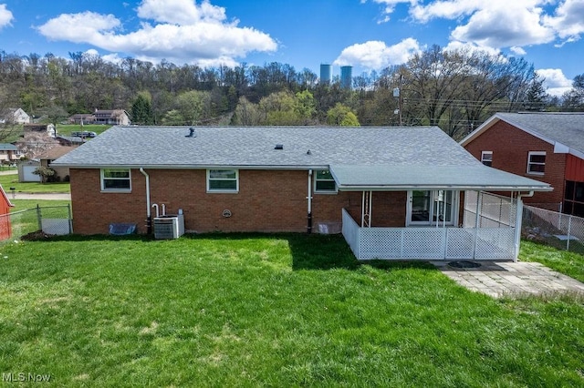 back of house with central AC unit, brick siding, fence, and a yard