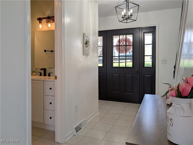 foyer with a chandelier, visible vents, light tile patterned flooring, and baseboards