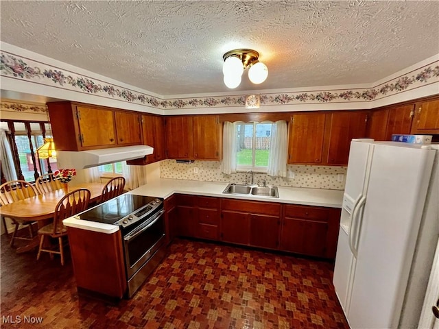 kitchen with a sink, white refrigerator with ice dispenser, stainless steel range with electric cooktop, light countertops, and a peninsula