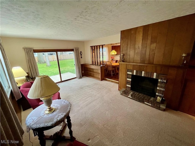 living area with wood walls, a brick fireplace, a textured ceiling, and carpet