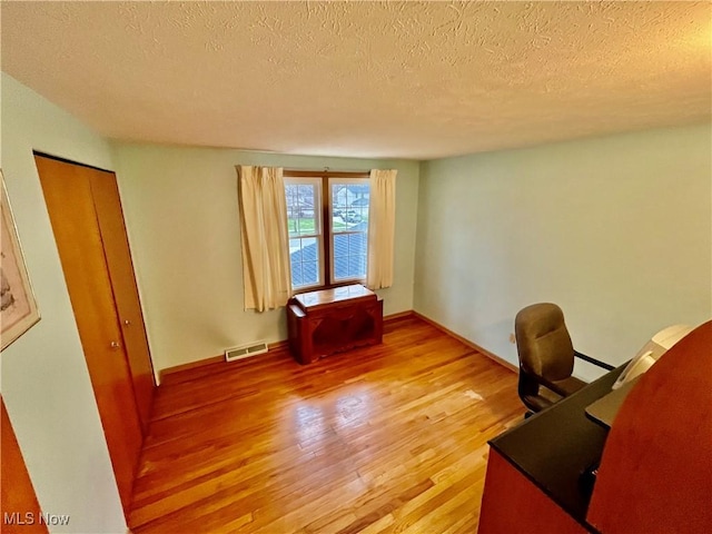 office area featuring baseboards, visible vents, a textured ceiling, and light wood finished floors