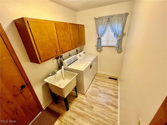 clothes washing area featuring light wood-style flooring, visible vents, baseboards, independent washer and dryer, and cabinet space