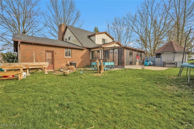 back of house featuring a trampoline, a chimney, a lawn, brick siding, and a sunroom
