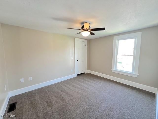 empty room with ceiling fan, baseboards, dark colored carpet, and visible vents