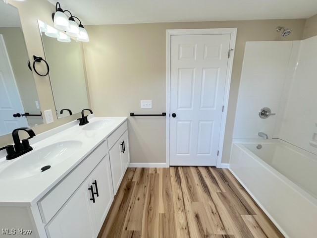 full bath featuring double vanity, wood finished floors, a sink, and  shower combination