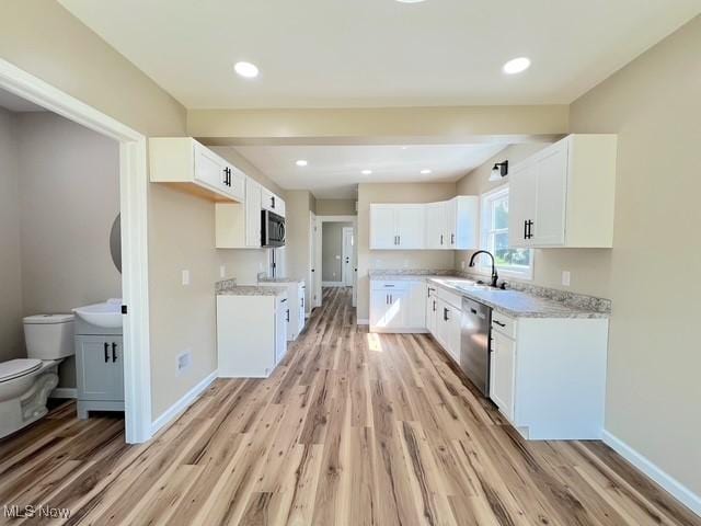 kitchen with dishwasher, white cabinetry, a sink, and light wood-type flooring