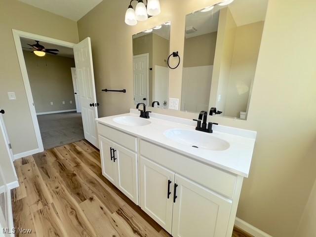bathroom with a ceiling fan, wood finished floors, a sink, and double vanity