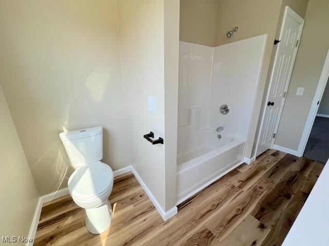 bathroom featuring baseboards, wood finished floors, washtub / shower combination, and toilet
