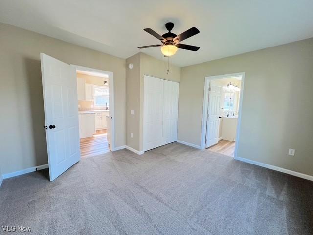 unfurnished bedroom with a ceiling fan, ensuite bathroom, a closet, light carpet, and baseboards