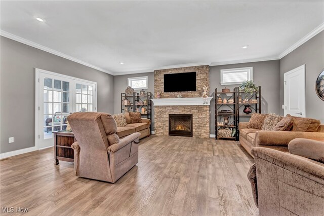 living area featuring light wood finished floors, baseboards, recessed lighting, a stone fireplace, and ornamental molding
