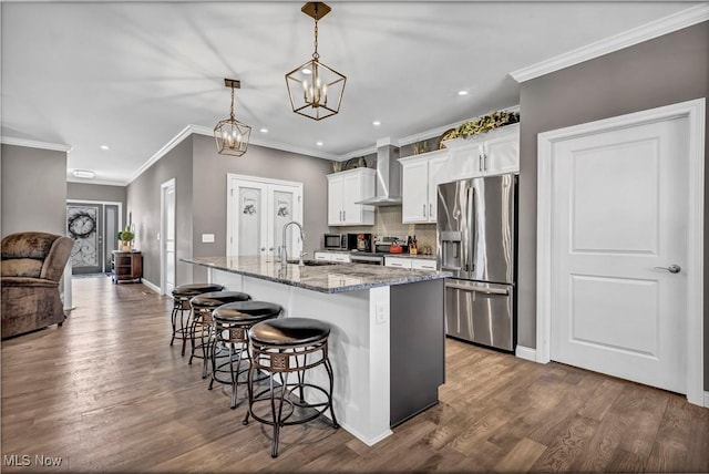 kitchen featuring wall chimney range hood, a center island with sink, a kitchen bar, appliances with stainless steel finishes, and recessed lighting