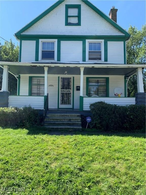 traditional style home featuring a chimney, a front yard, and covered porch
