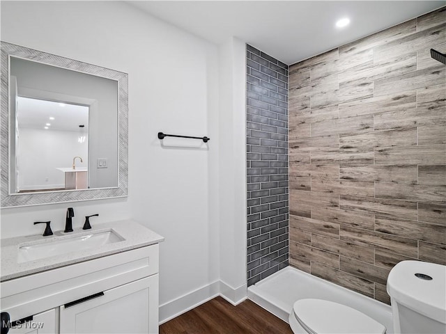 full bath featuring wood finished floors, toilet, vanity, baseboards, and tiled shower