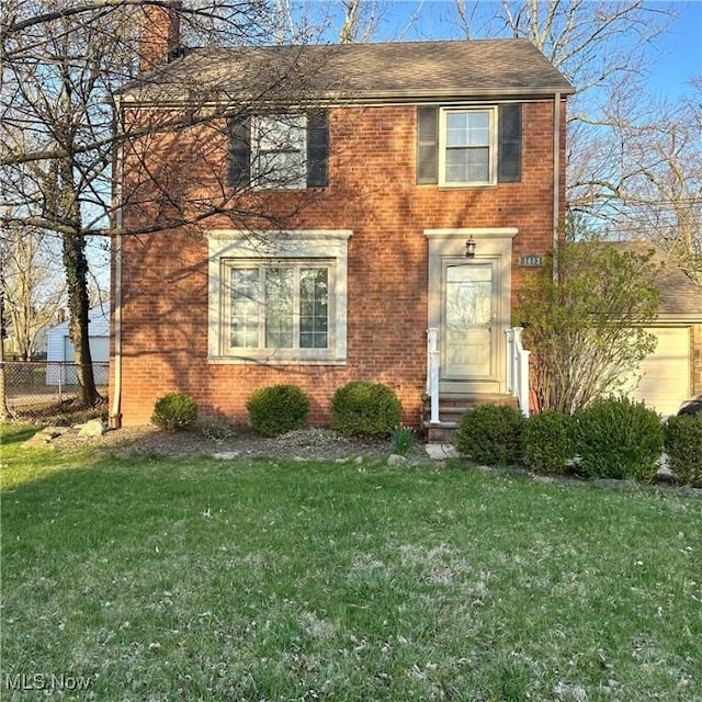 view of front facade with a front lawn, a shingled roof, a chimney, brick siding, and fence