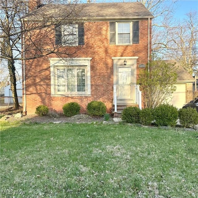 colonial home featuring a front yard, fence, roof with shingles, and brick siding