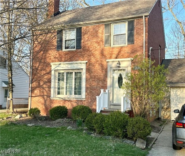 colonial home with a shingled roof, a garage, a chimney, brick siding, and fence