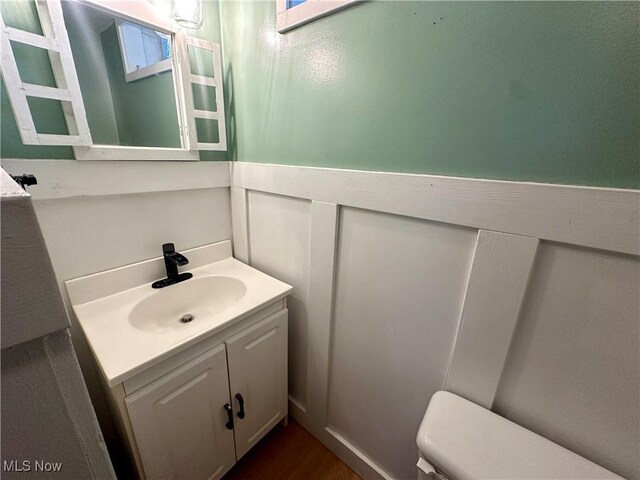half bath with toilet, wood finished floors, and vanity
