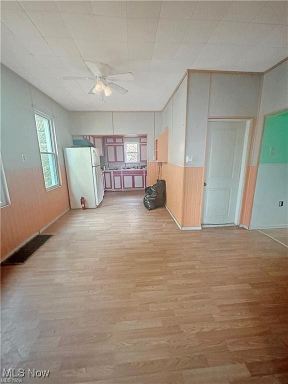 spare room featuring a wainscoted wall, wooden walls, visible vents, light wood-style flooring, and ceiling fan