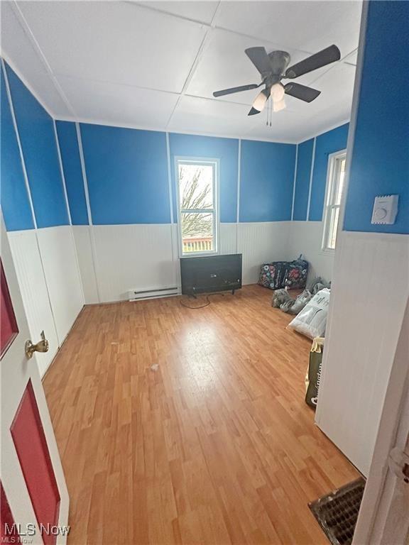 empty room with wainscoting, ceiling fan, a baseboard radiator, and light wood-type flooring
