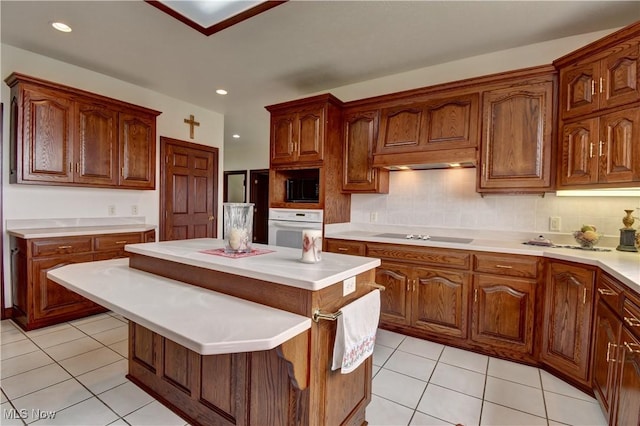 kitchen with tasteful backsplash, black appliances, light tile patterned floors, light countertops, and a kitchen island