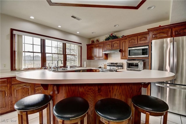 kitchen with stainless steel appliances, a sink, visible vents, light countertops, and under cabinet range hood