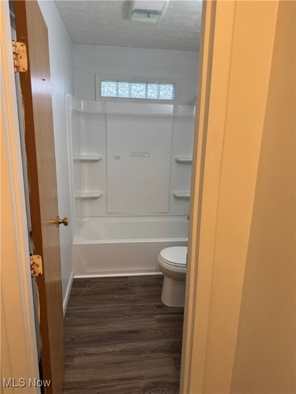 bathroom with a textured ceiling, toilet, visible vents, wood finished floors, and washtub / shower combination