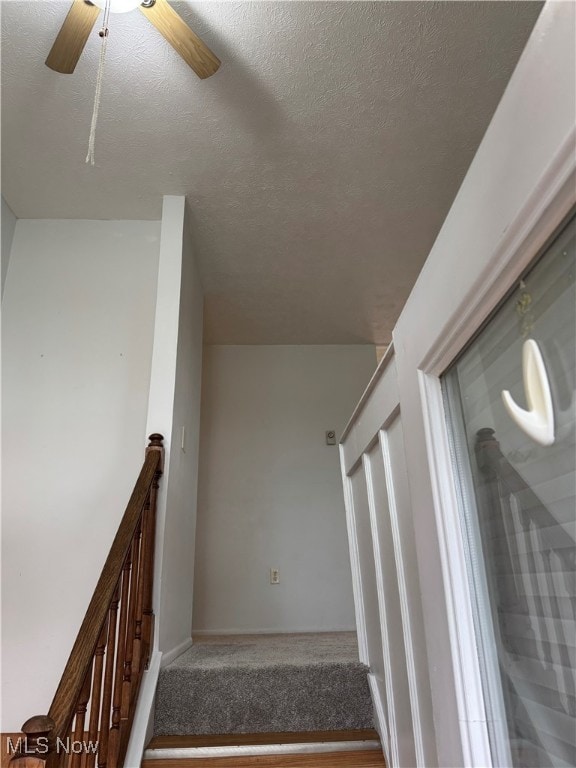 staircase featuring a ceiling fan, baseboards, a textured ceiling, and carpet floors