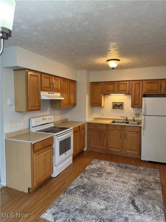 kitchen featuring under cabinet range hood, wood finished floors, a sink, white appliances, and brown cabinetry
