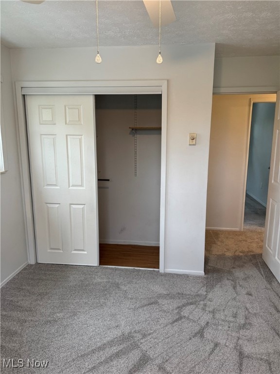 unfurnished bedroom with a textured ceiling, carpet floors, a closet, and baseboards