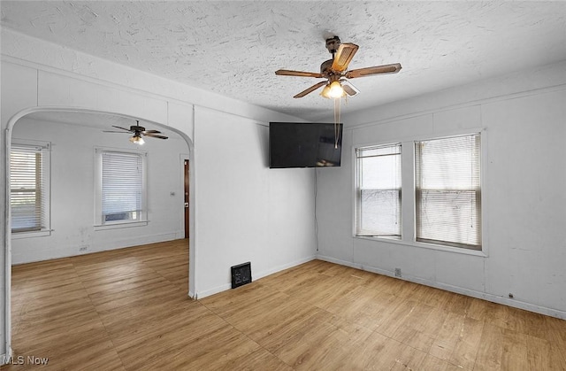 spare room featuring arched walkways, plenty of natural light, a textured ceiling, and a ceiling fan
