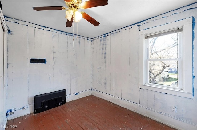 unfurnished room featuring wood-type flooring, wooden walls, and ceiling fan