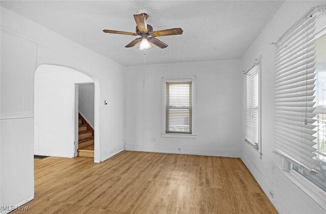 spare room with arched walkways, light wood-style floors, plenty of natural light, and ceiling fan