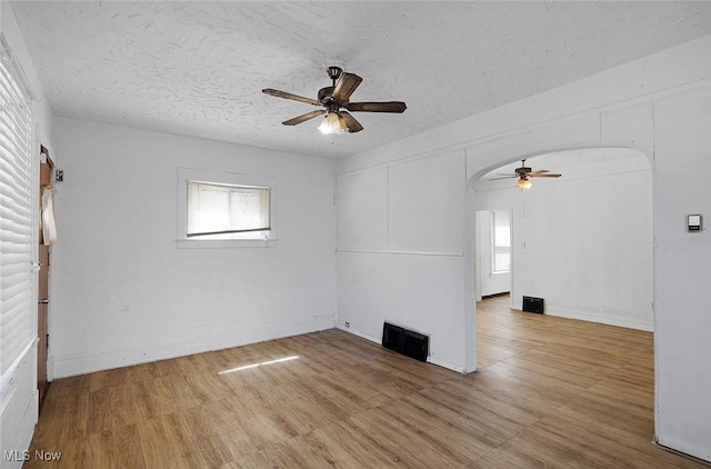 unfurnished room with light wood-style flooring, visible vents, arched walkways, and ceiling fan