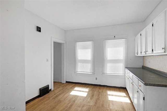 unfurnished dining area with light wood-style flooring, visible vents, and baseboards