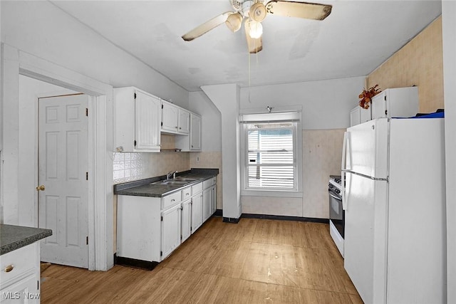 kitchen with white cabinets, a sink, dark countertops, white appliances, and ceiling fan