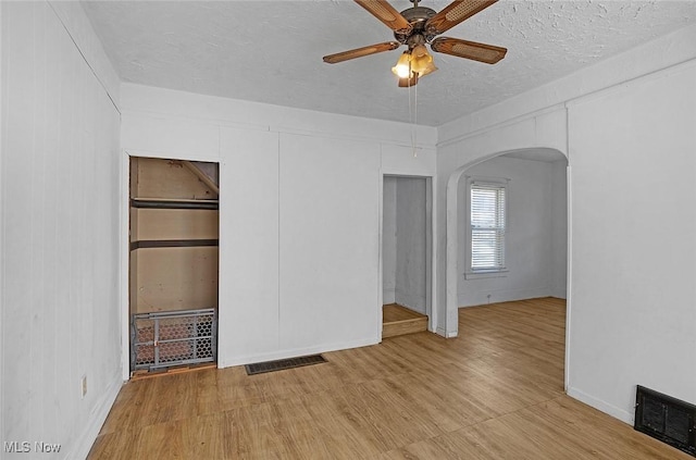 unfurnished bedroom featuring wood finished floors, visible vents, arched walkways, and a textured ceiling