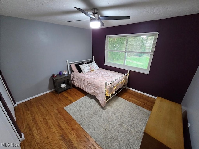 bedroom with wood finished floors, a textured ceiling, baseboards, and ceiling fan