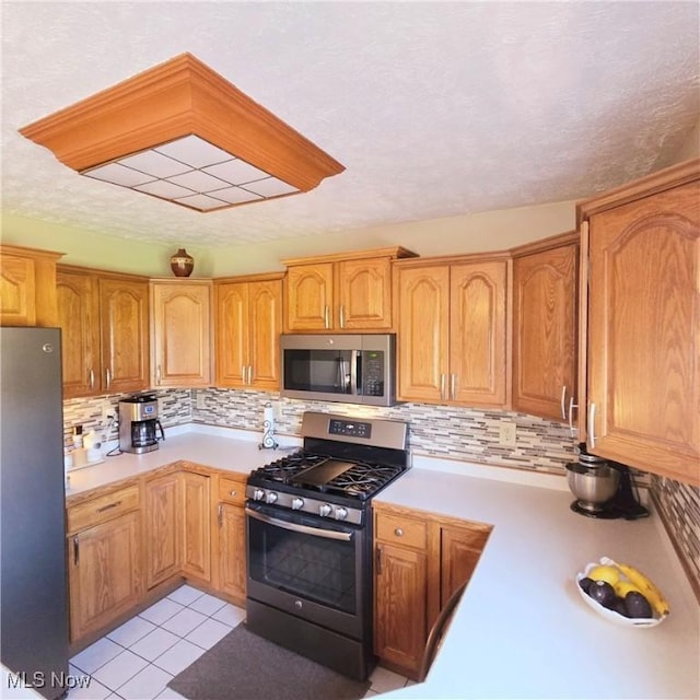kitchen with stainless steel appliances, light countertops, decorative backsplash, and light tile patterned flooring