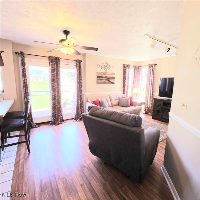 living room featuring track lighting, wood finished floors, ceiling fan, and a healthy amount of sunlight