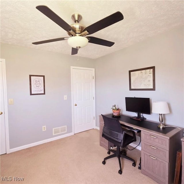 home office with a ceiling fan, a textured ceiling, light carpet, baseboards, and visible vents
