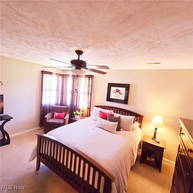 bedroom featuring carpet flooring, a textured ceiling, visible vents, baseboards, and a ceiling fan